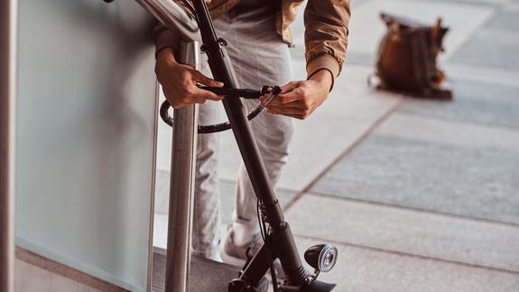© Envato Elements Mann schließt E-Scooter mit Schloss an